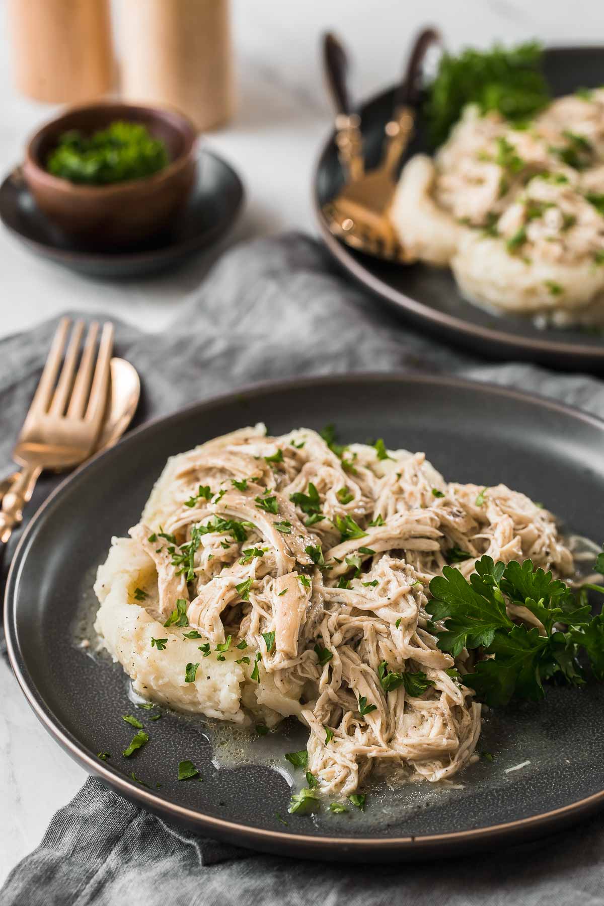 Two plates of shredded chicken over mashed potatoes.