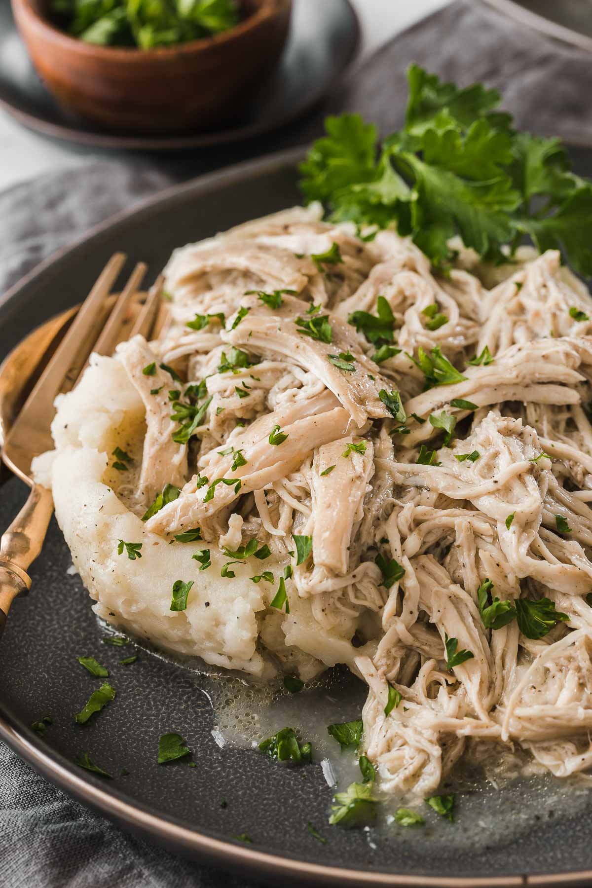 Grey plate with shredded chicken over mashed potatoes.