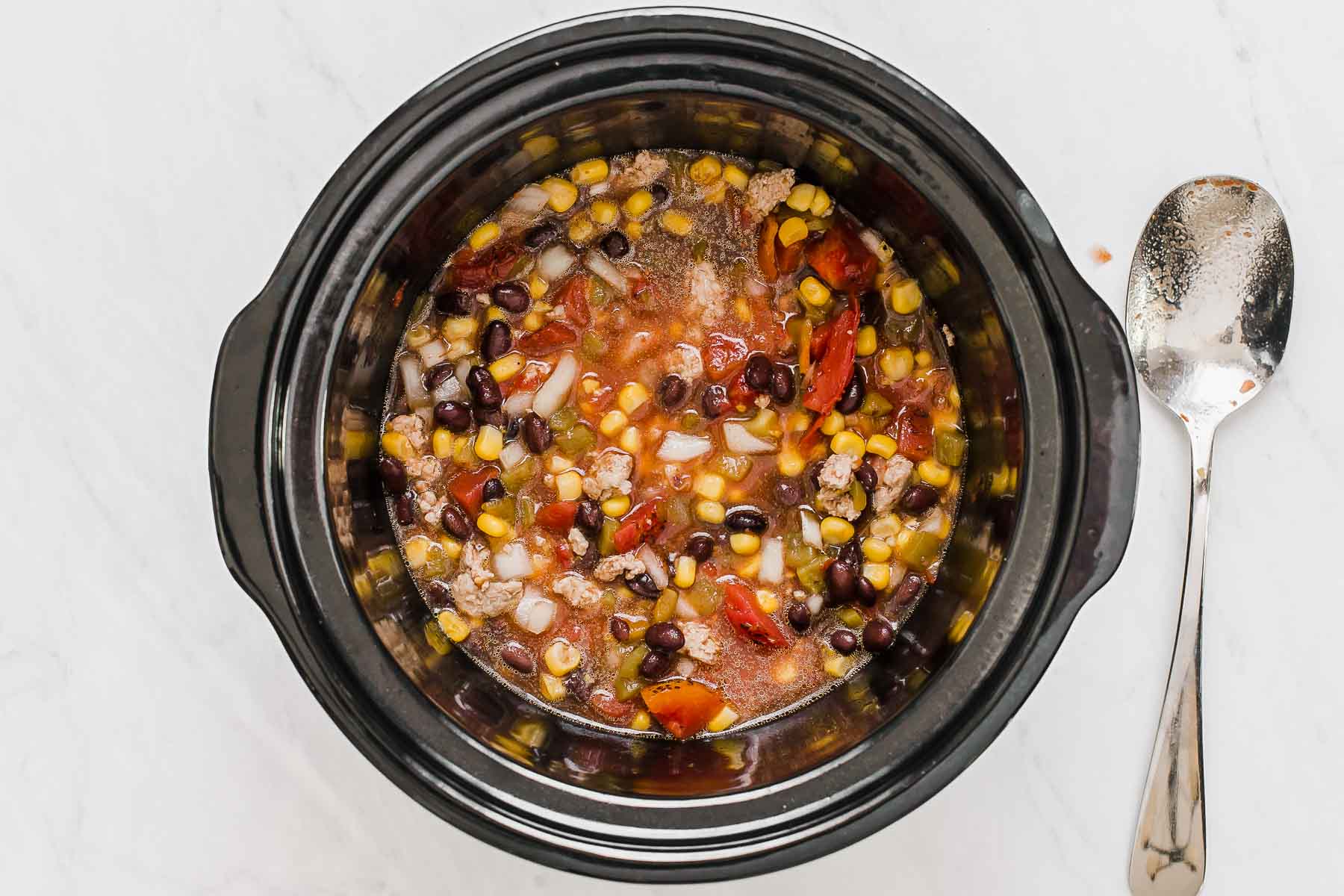 Soup with black beans, corn and tomatoes in black crockpot.