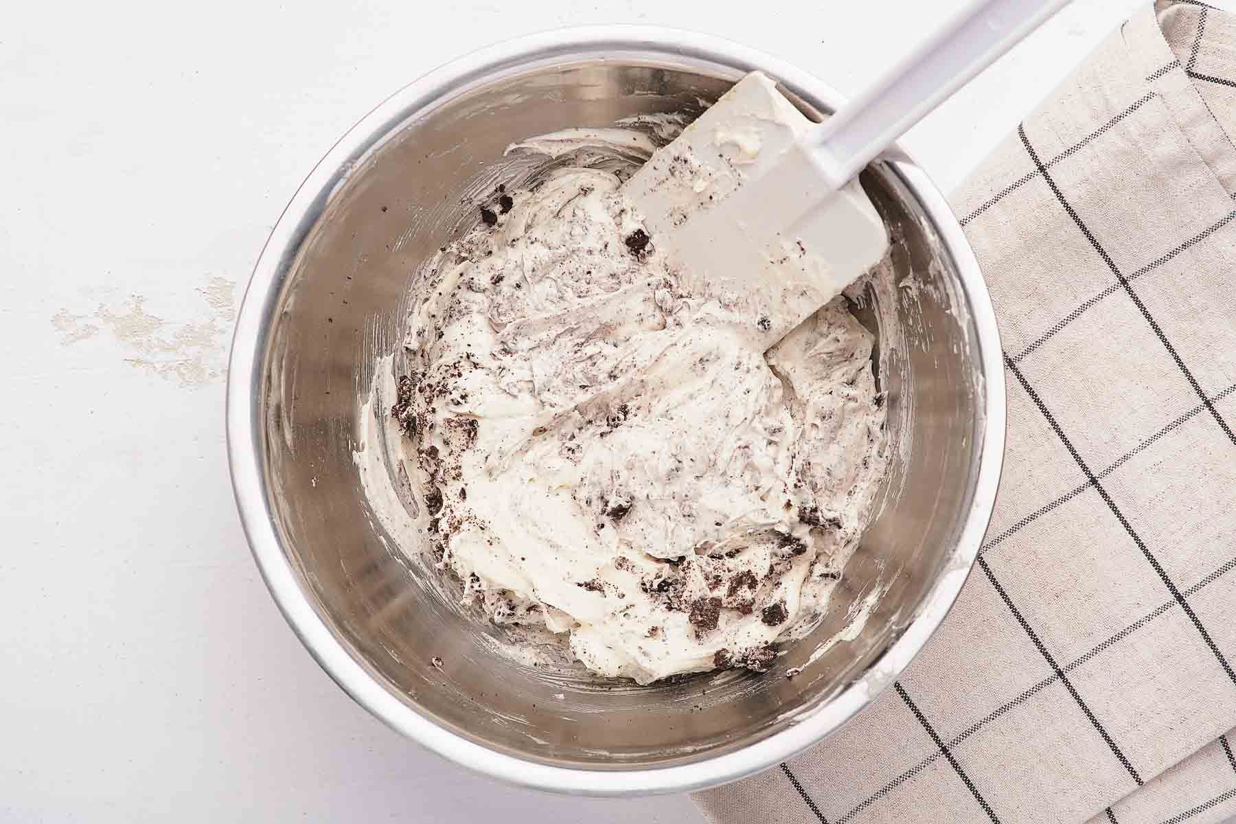 Stirring crushed cookies into white fluffy dessert with spatula.