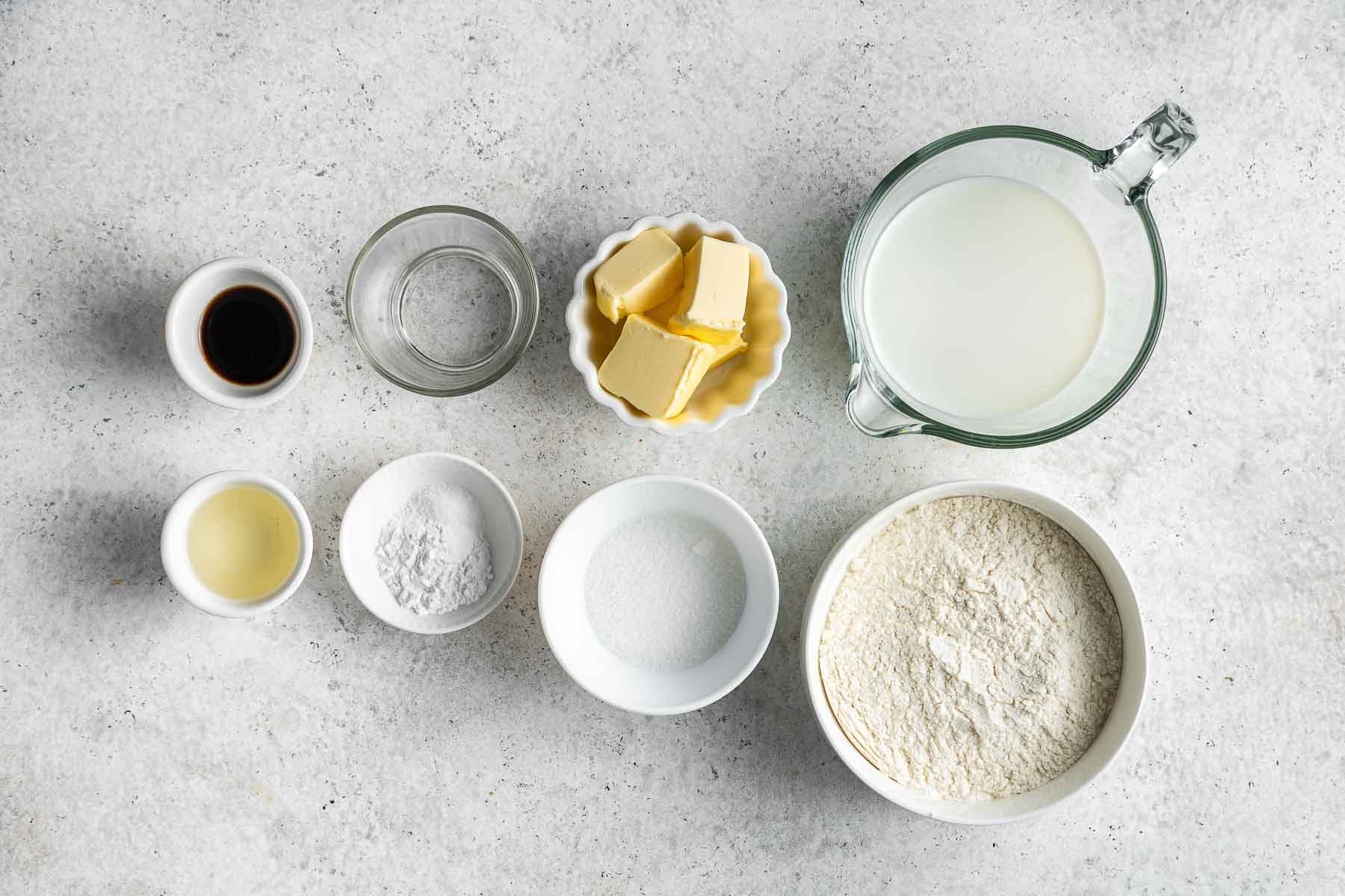Ingredients for eggless pancakes in little bowls on white surface.