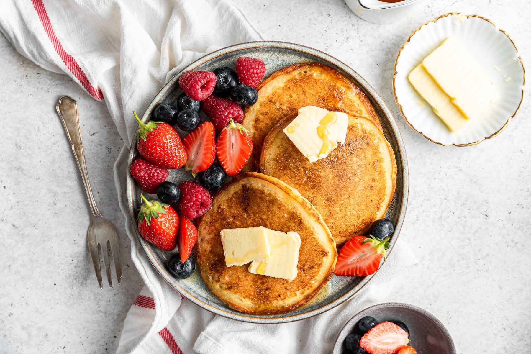 Plate of pancakes topped with butter and fresh berries.