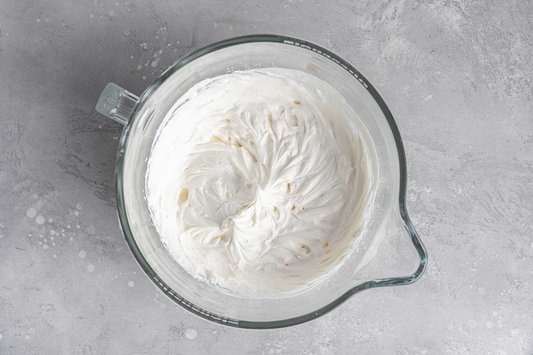 Whipped cream cream cheese frosting in clear mixing bowl.