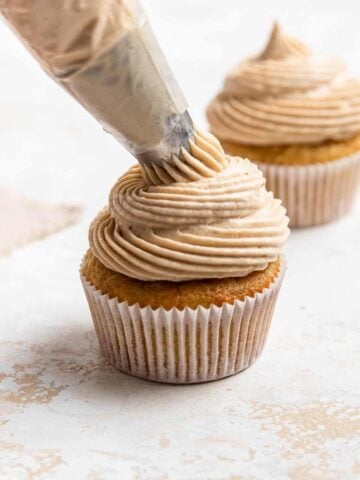 Piping bag adding brown sugar cream cheese frosting to a cupcake.
