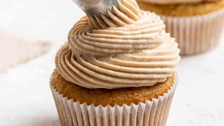 Piping bag adding brown sugar cream cheese frosting to a cupcake.