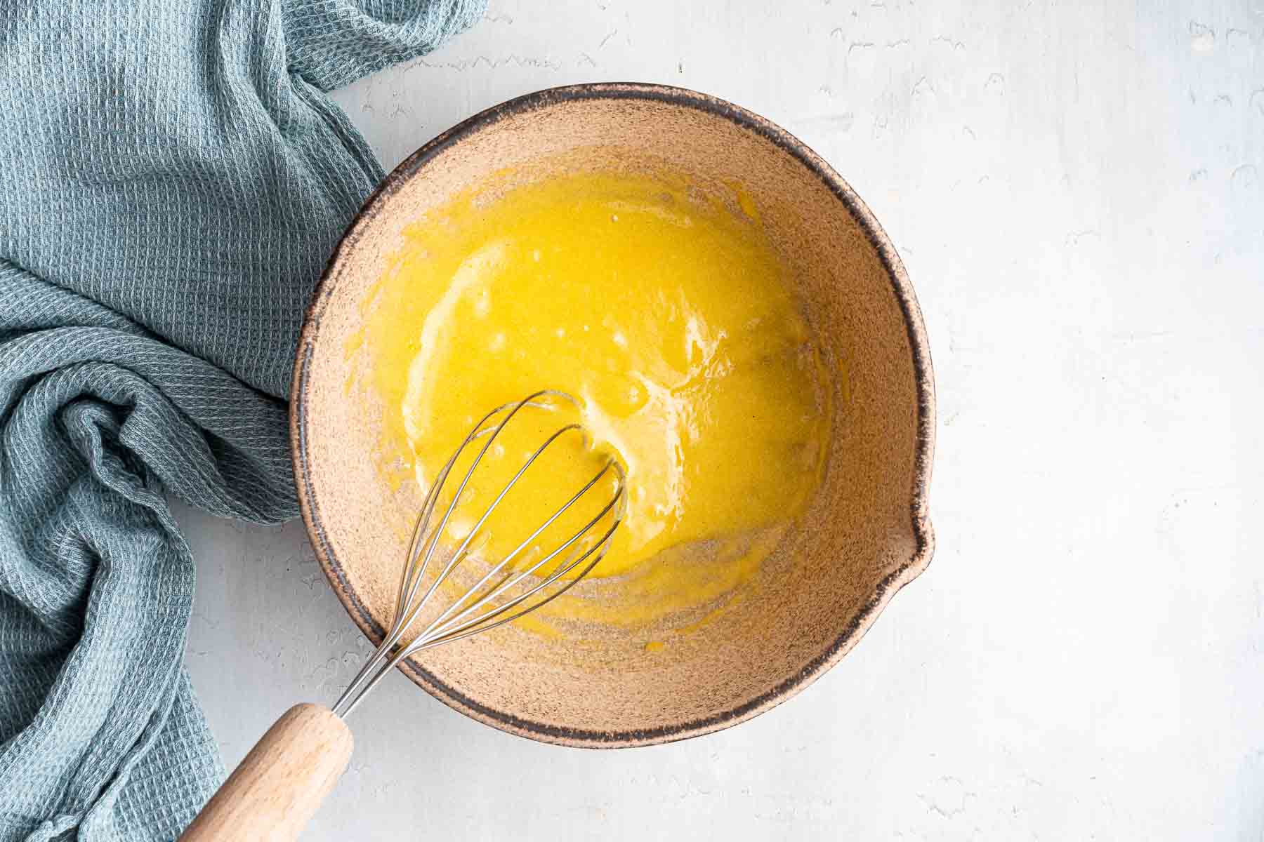 Mixing bowl with bright yellow liquid and whisk.