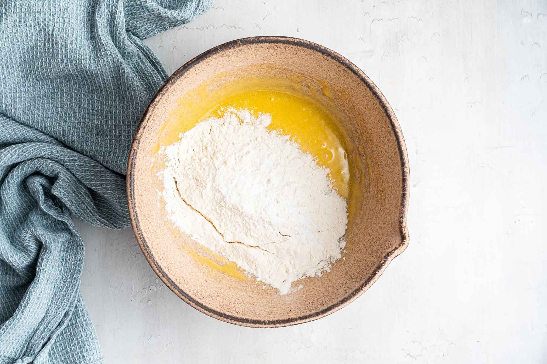 Mixing bowl with yellow batter with flour on top.
