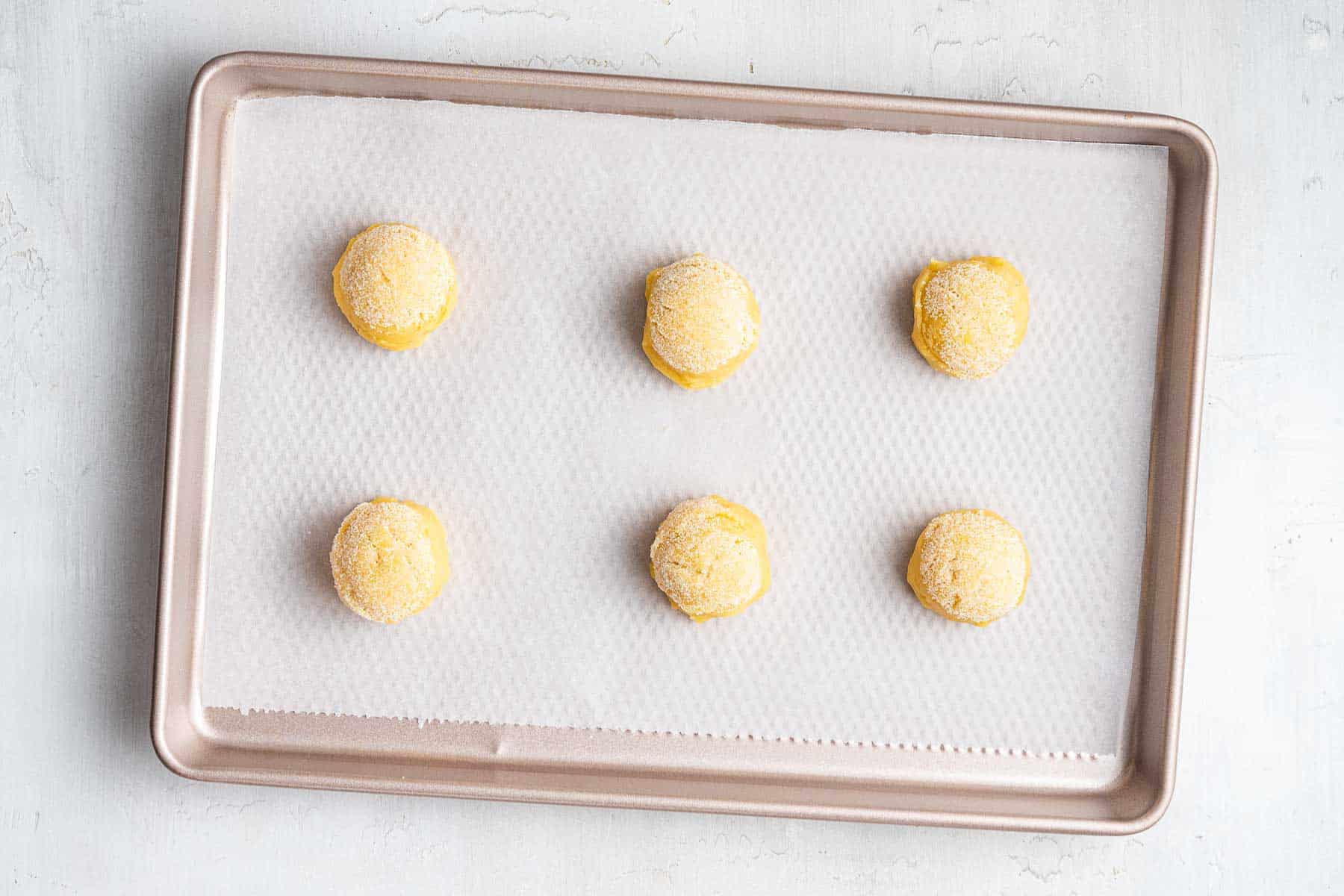 Six yellow dough balls on baking sheet covered with parchment paper.