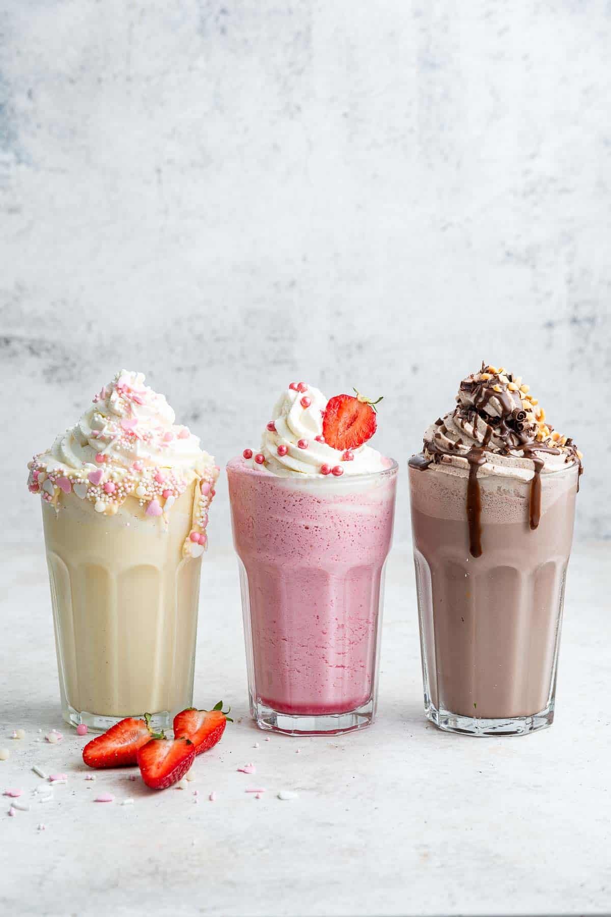 Vertical image of 3 milkshakes: vanilla, strawberry and chocolate.