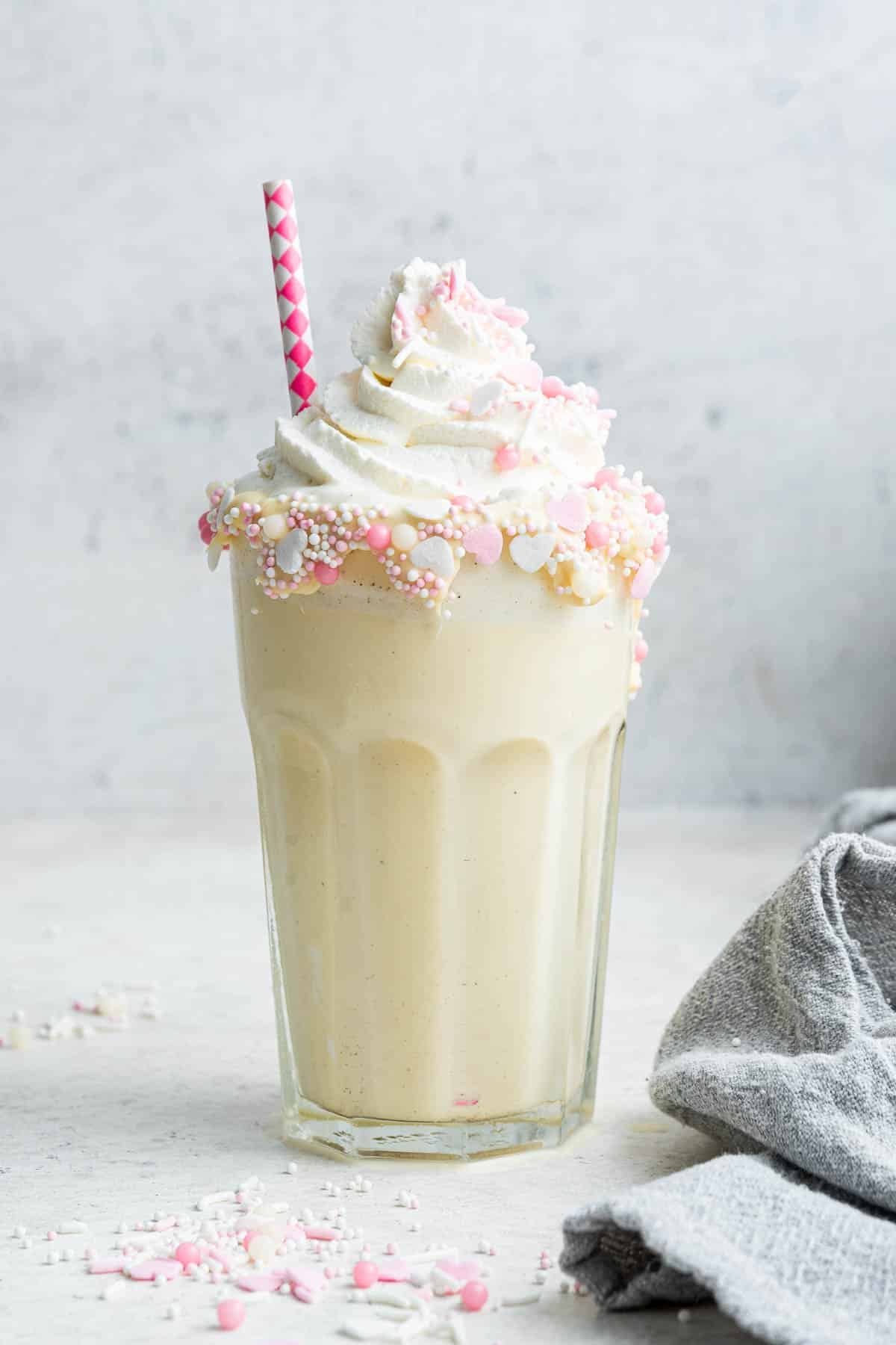 Vanilla dessert drink in glass with whipped cream, sprinkles and a straw.