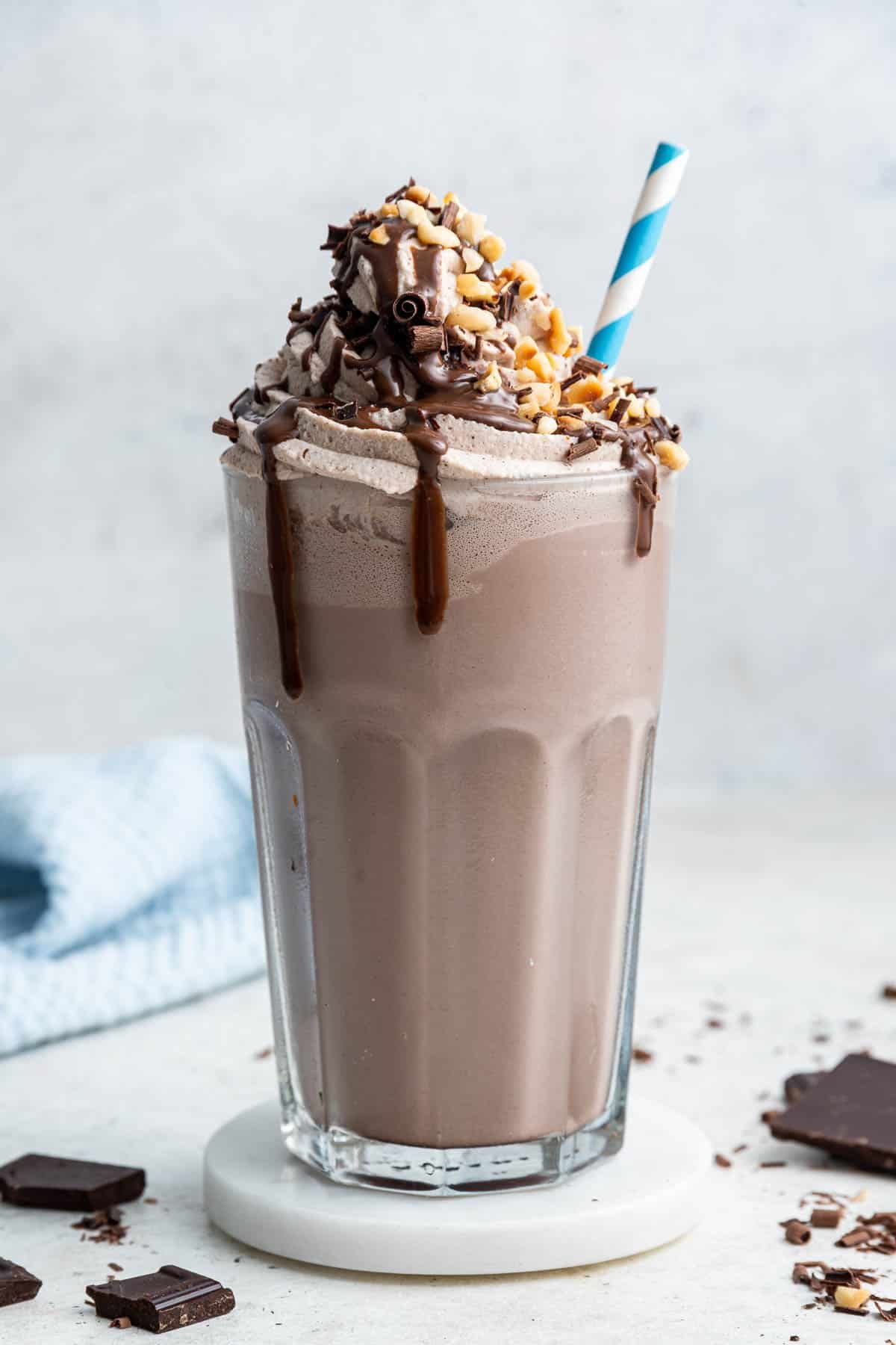 Chocolate milkshake in glass with whipped cream, chocolate drizzle and straw.