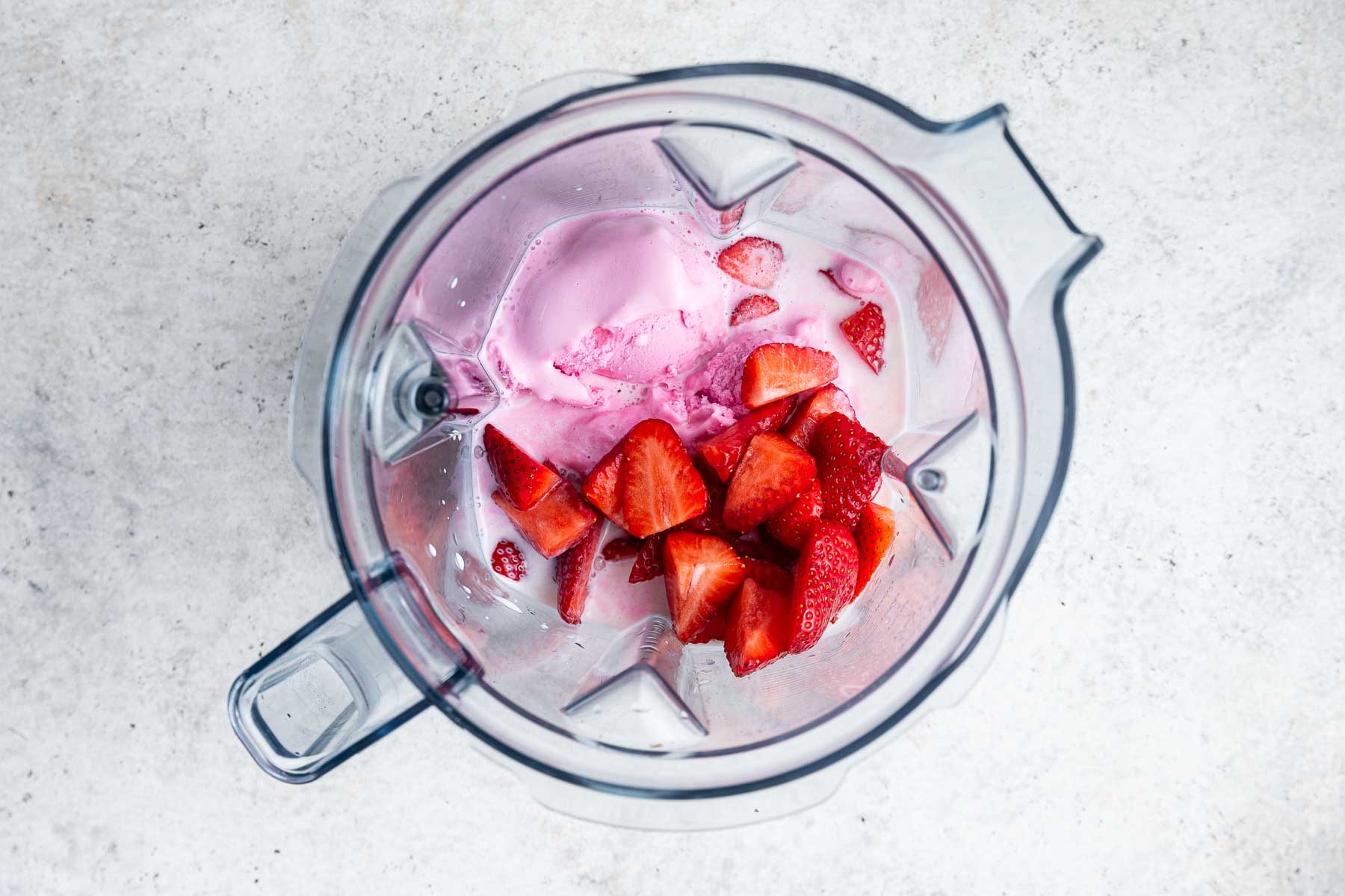 Blender with scoops of strawberry ice cream, strawberries and milk.