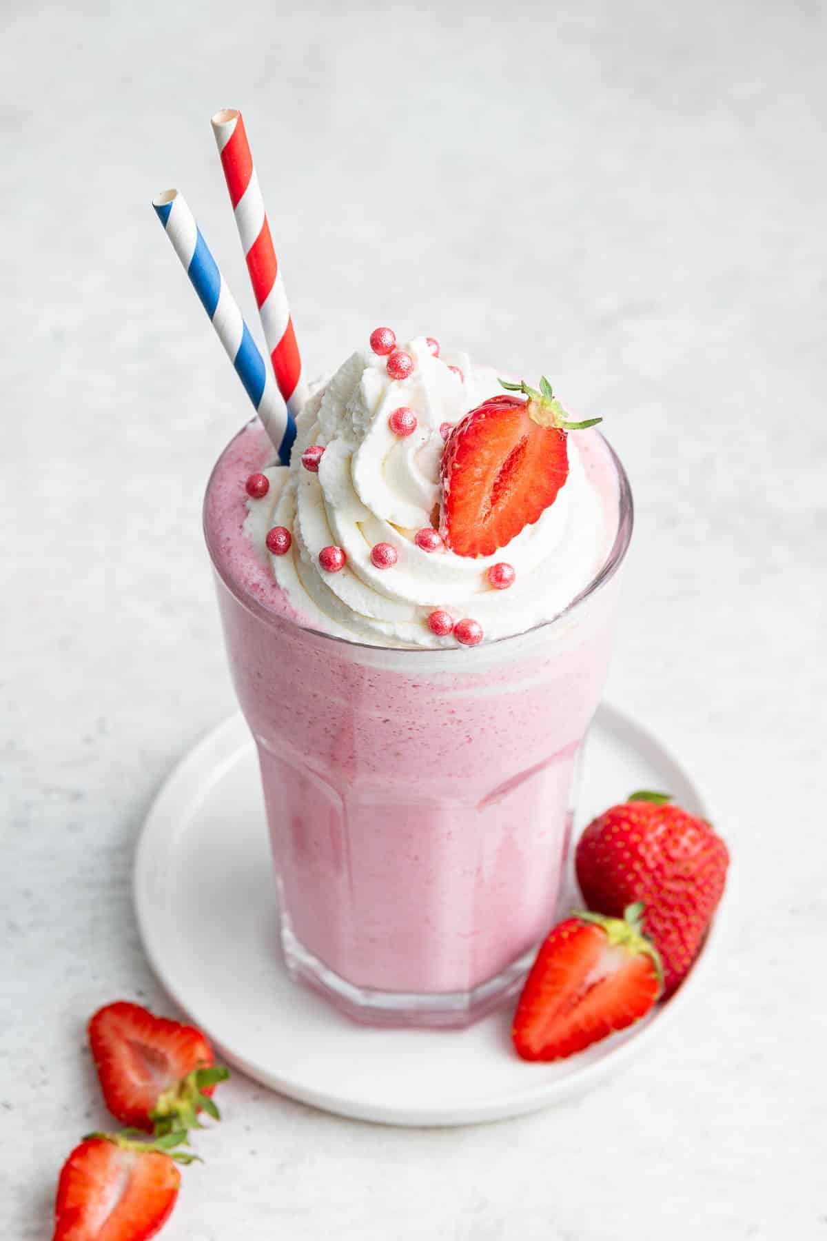 Best milkshake recipe for strawberries in a glass, garnished with 2 straws.