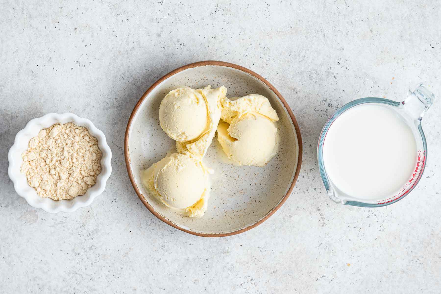 Three plates with scoops of vanilla ice cream, milk and malted milk powder on counter.