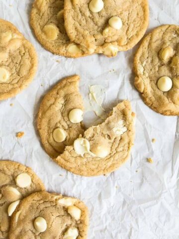 White chocolate chip cookies spread on a piece of white parchment paper.
