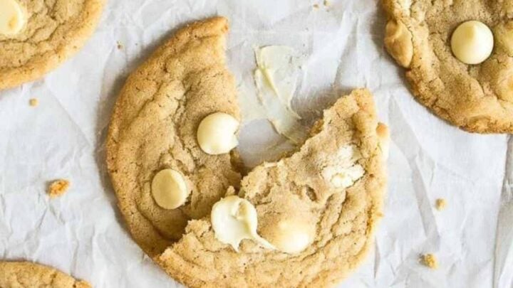 White chocolate chip cookies spread on a piece of white parchment paper.