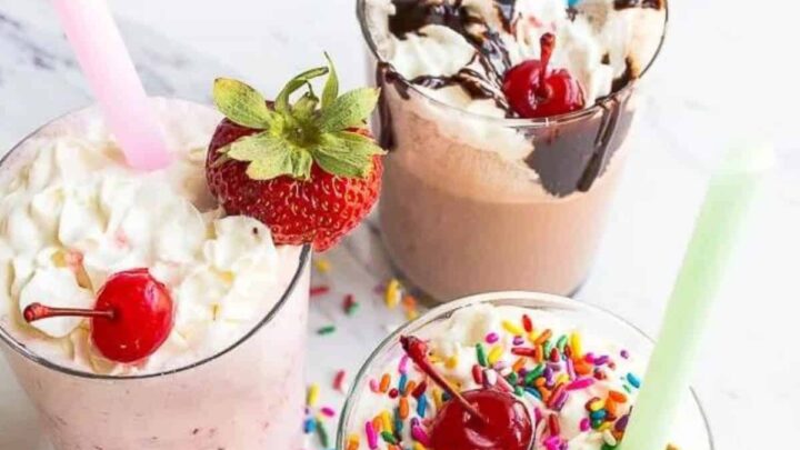 Three glasses with milkshakes, sprinkles and a cherry on top with straws.