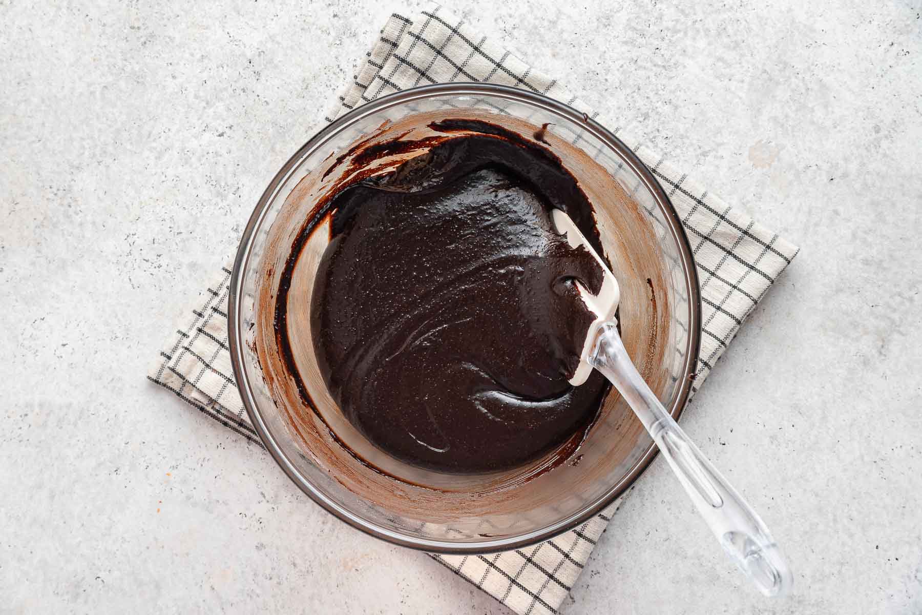 Raw eggless brownie batter in glass bowl with spatula.