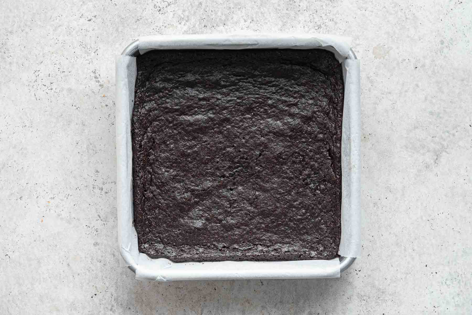 Freshly baked brownies in a square pan lined with white parchment paper.