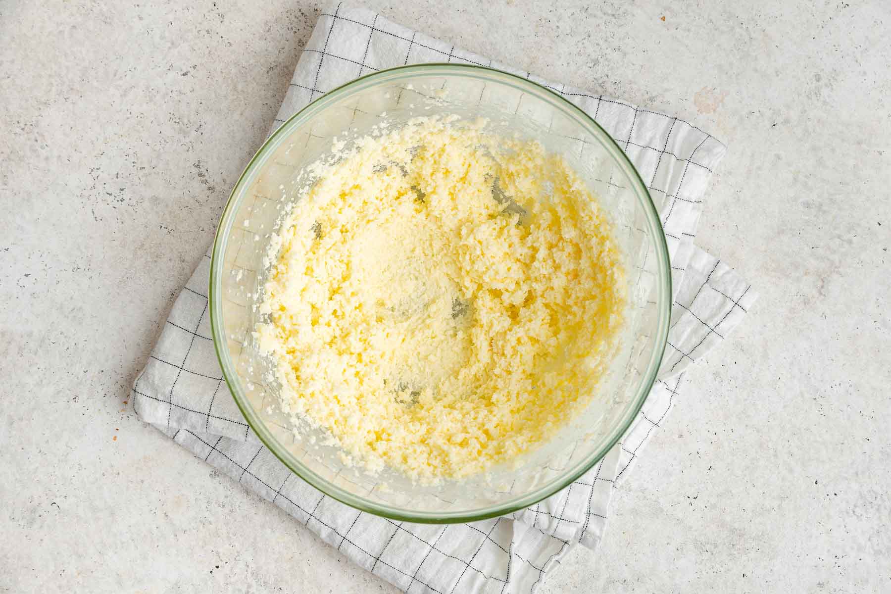 Bright yellow butter and granulated sugar beaten together in clear glass bowl.