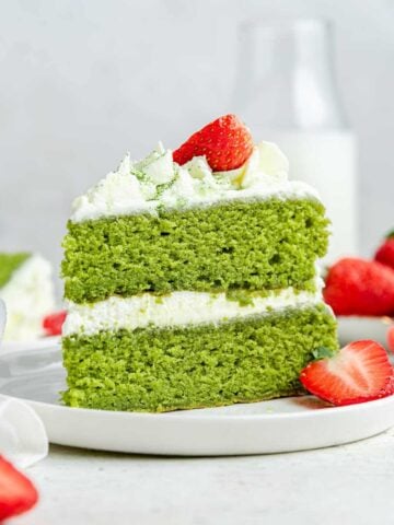 Up close vertical shot of bright green matcha cake with white frosting and fresh strawberries.
