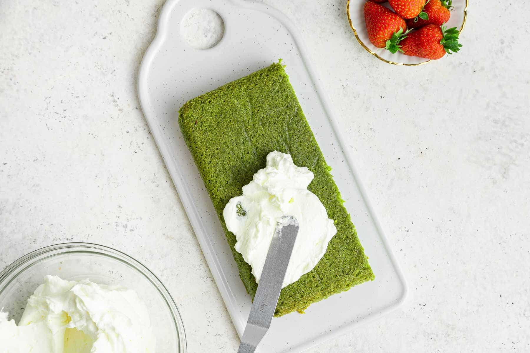 Rectangular green cake being spread with white frosting.
