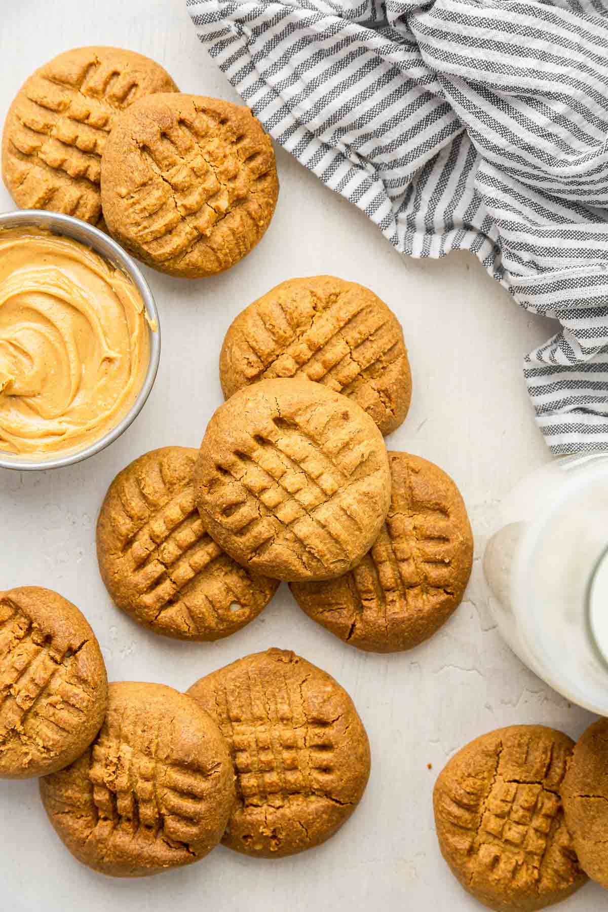 Criss cross 2 ingredient peanut butter cookies on white board with bowl of peanut butter.