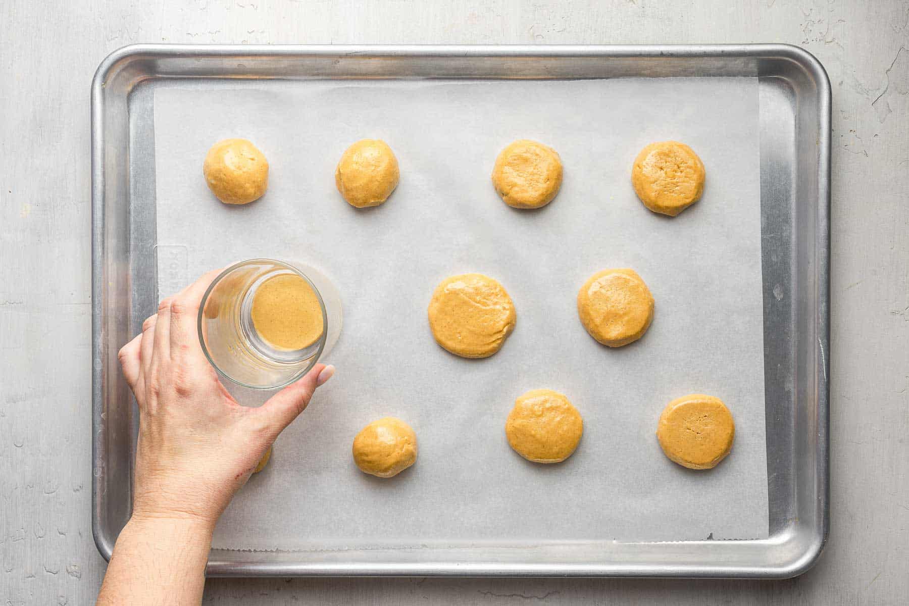Smashing cookies on sheet pan with glass cup.