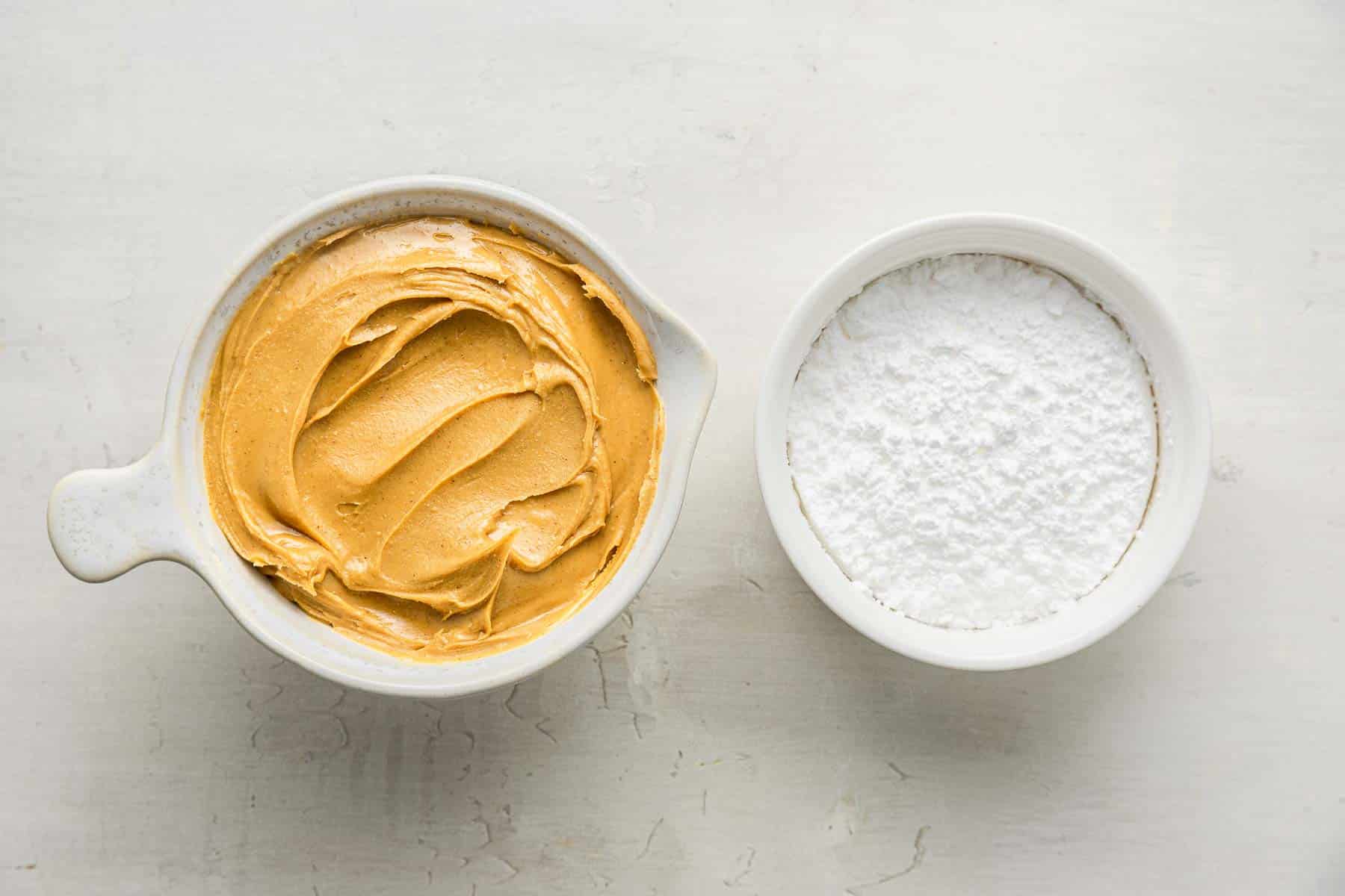 A bowl of peanut butter next to a bowl of powdered sugar.