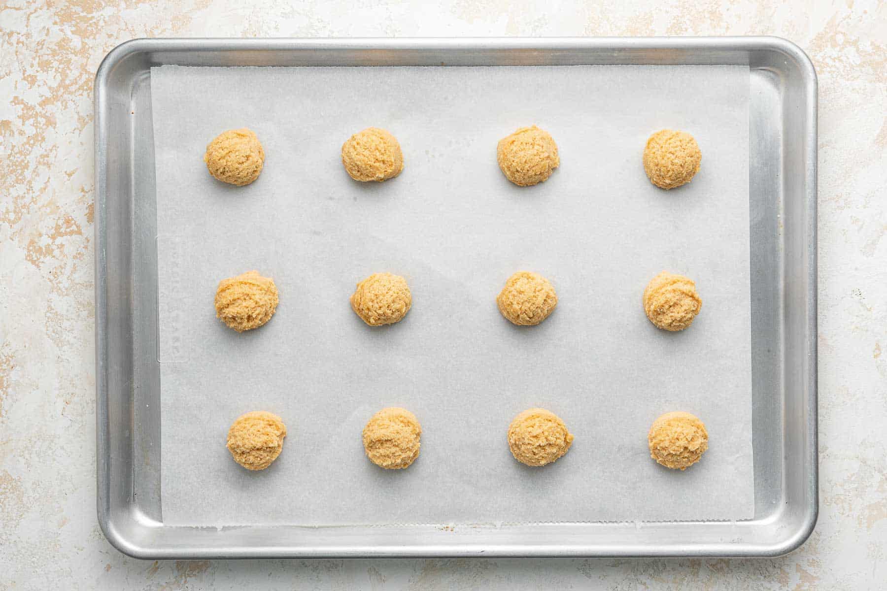 Twelve cookie dough balls on a baking sheet with parchment paper.