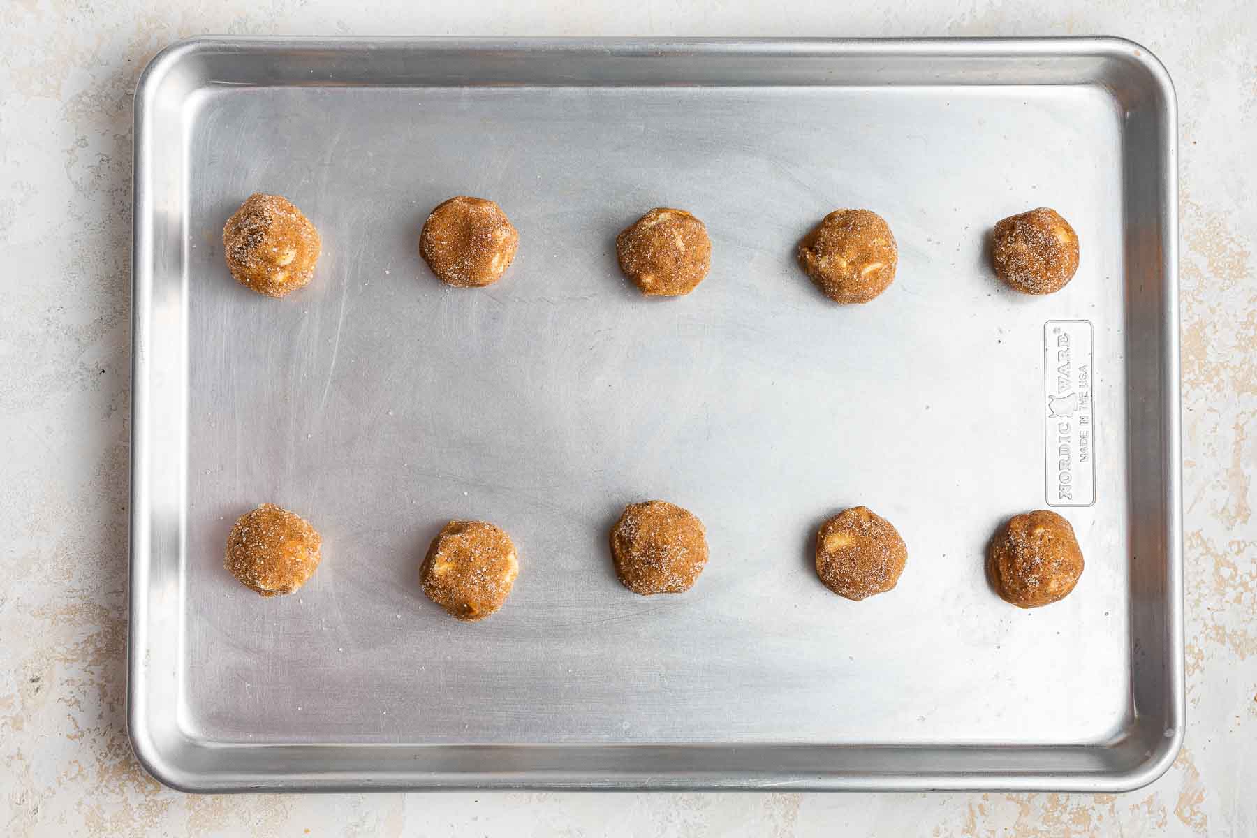 Ten pumpkin white chocolate chip cookies dough balls on silver baking sheet.