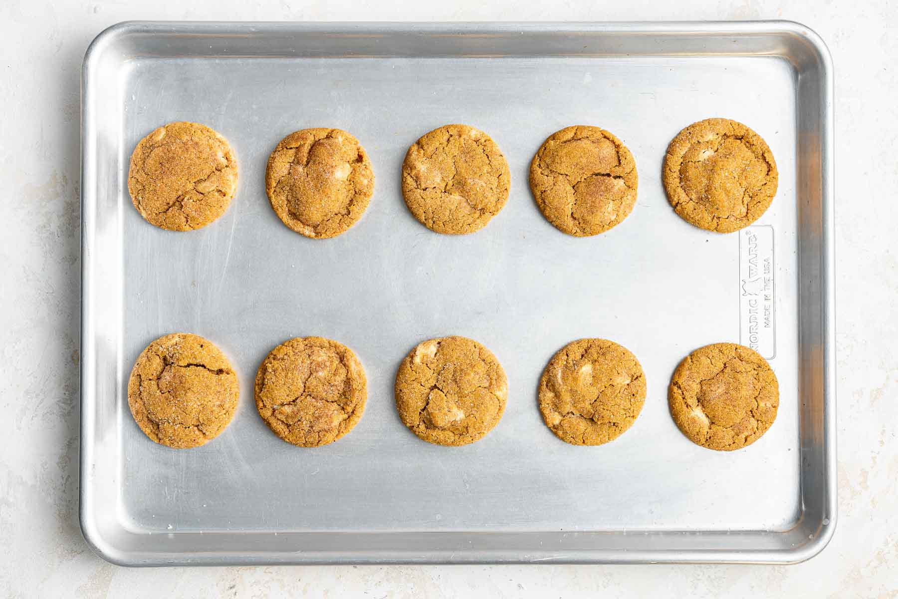 Ten freshly baked orange treats on silver cookie pan.