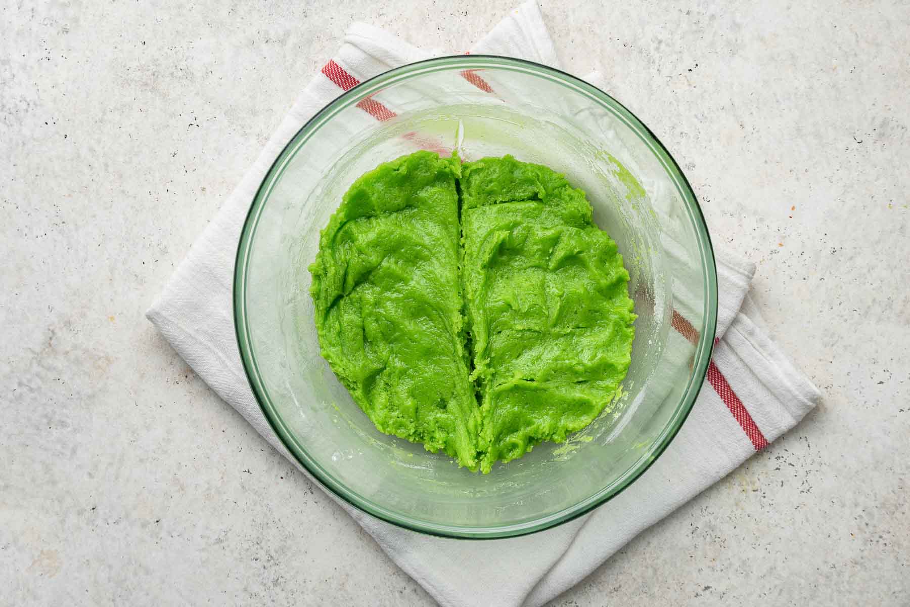 Bright green cookie dough in clear bowl with line drawn down middle.
