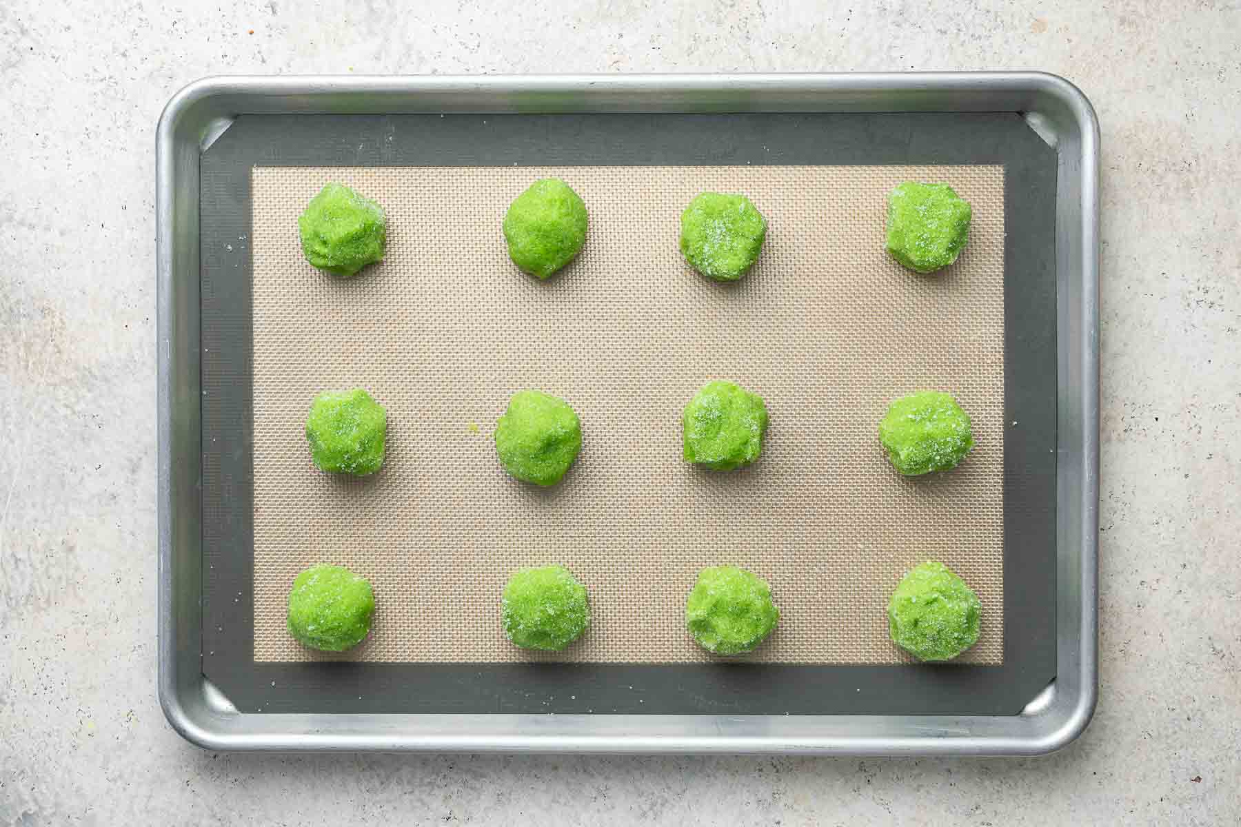 Twelve Grinch sugar cookies on baking sheet, before being baked.