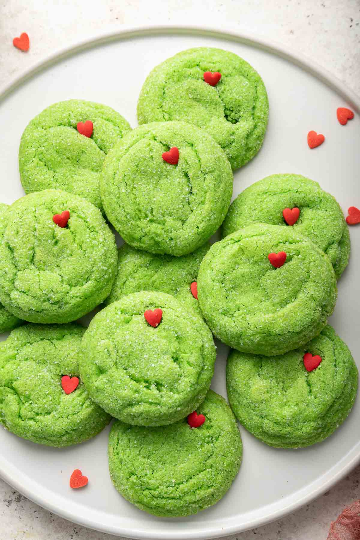 White plate of green grinch sugar cookies with small red hearts.