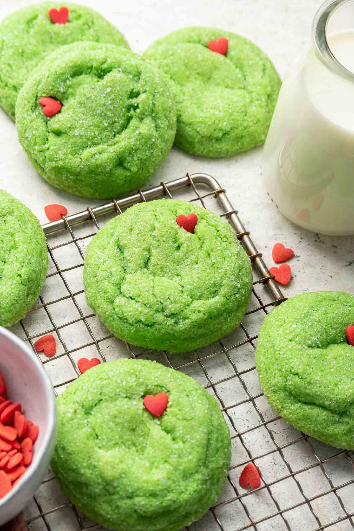 Green sugar cookies on tray with red sprinkles.