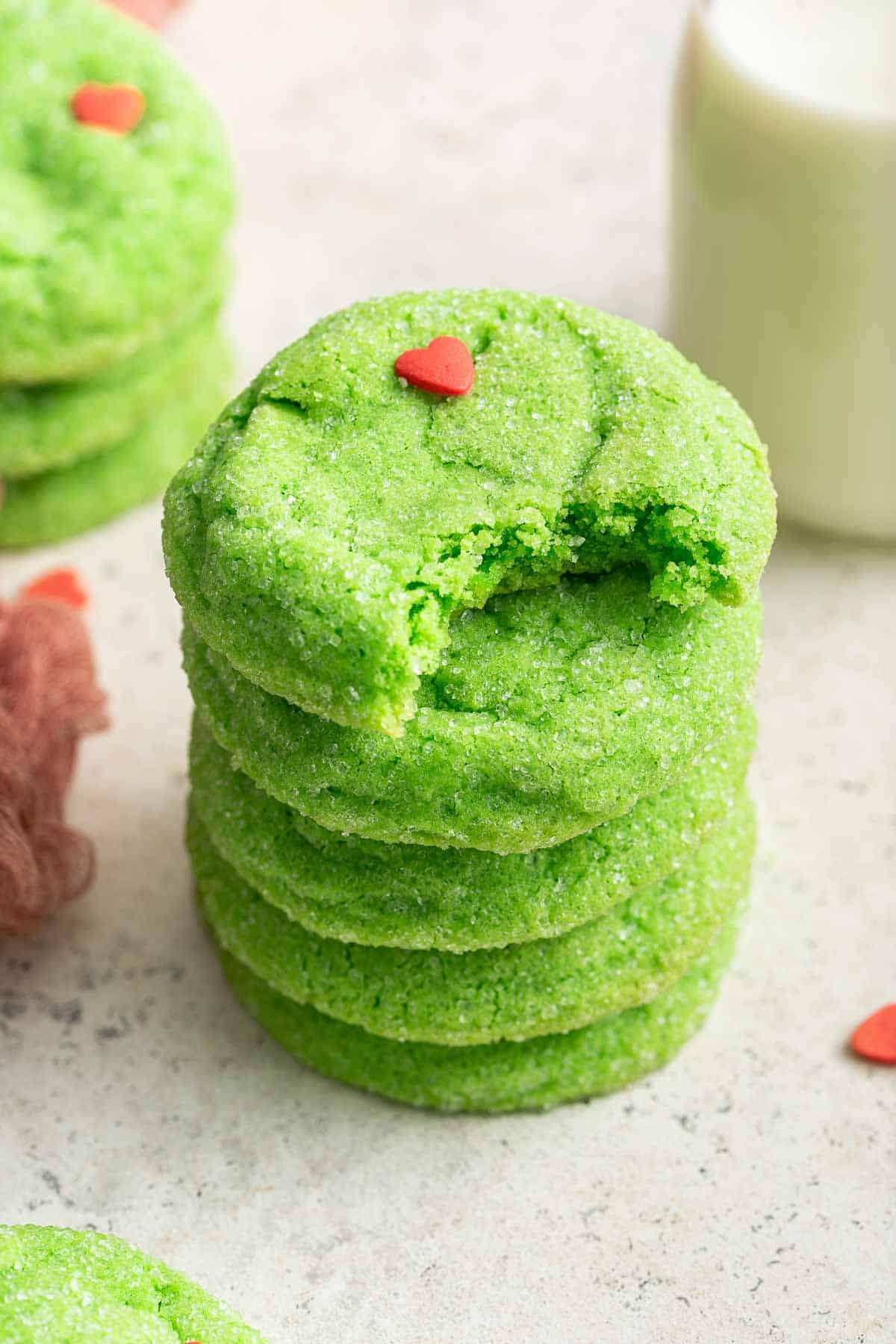 Stack of bright green Grinch cookies with heart sprinkle.