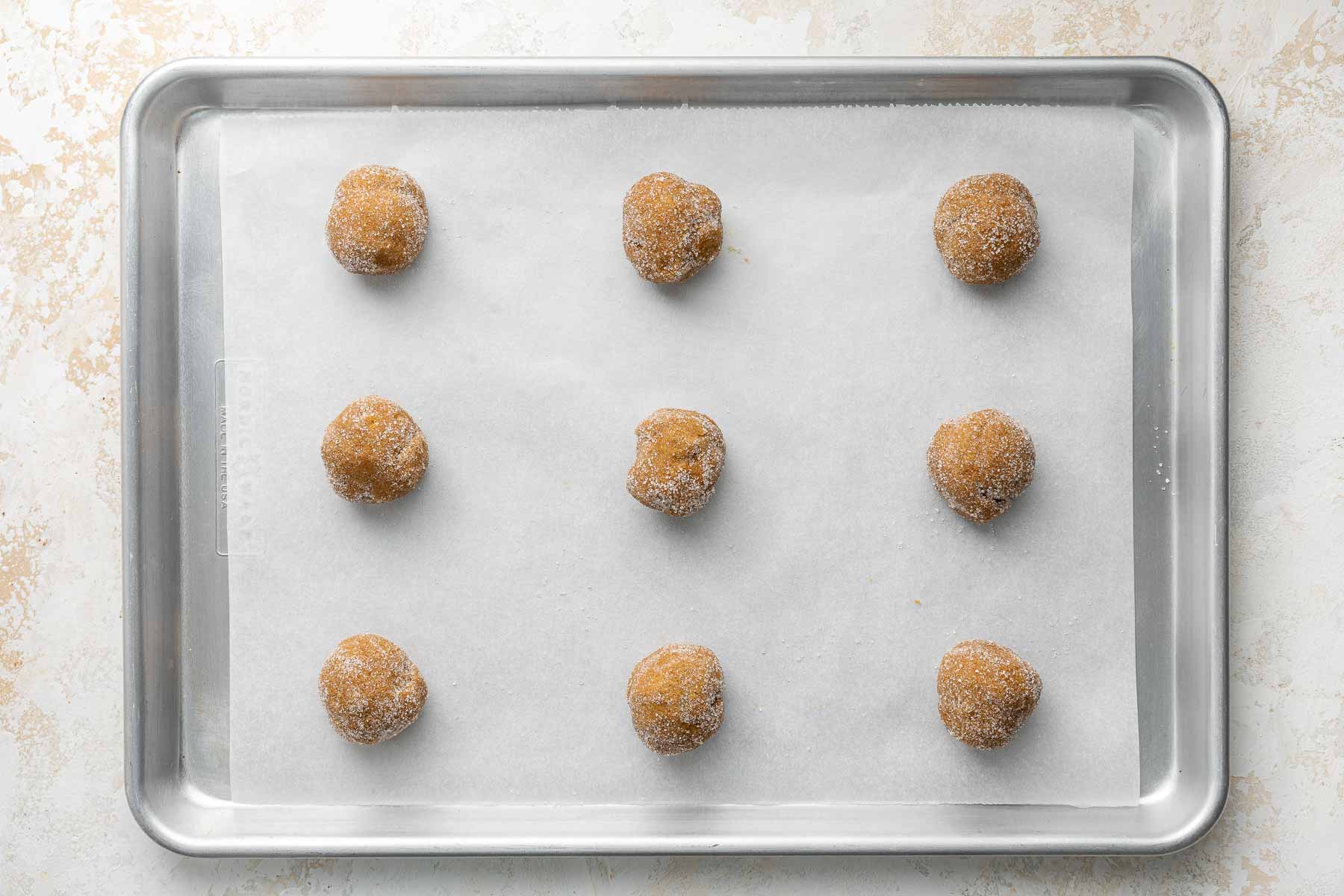Nine dough balls on a baking sheet before being baked.