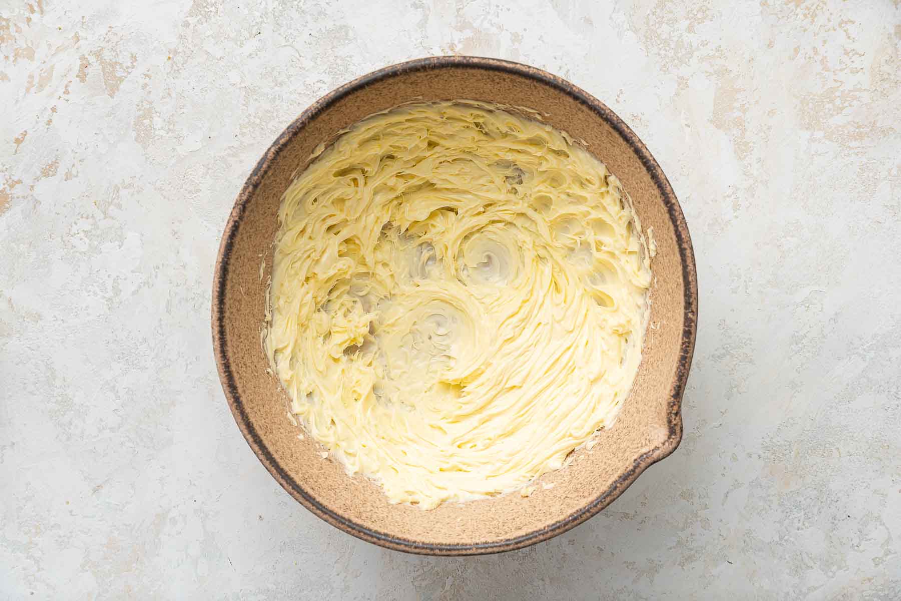 Butter and sugar creamed together in a brown pottery bowl.