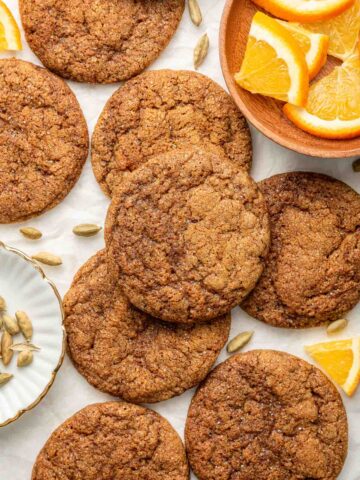 Overhead shot of brown crinkle cookies with orange slices and cardamom pods surrounding the cookies.