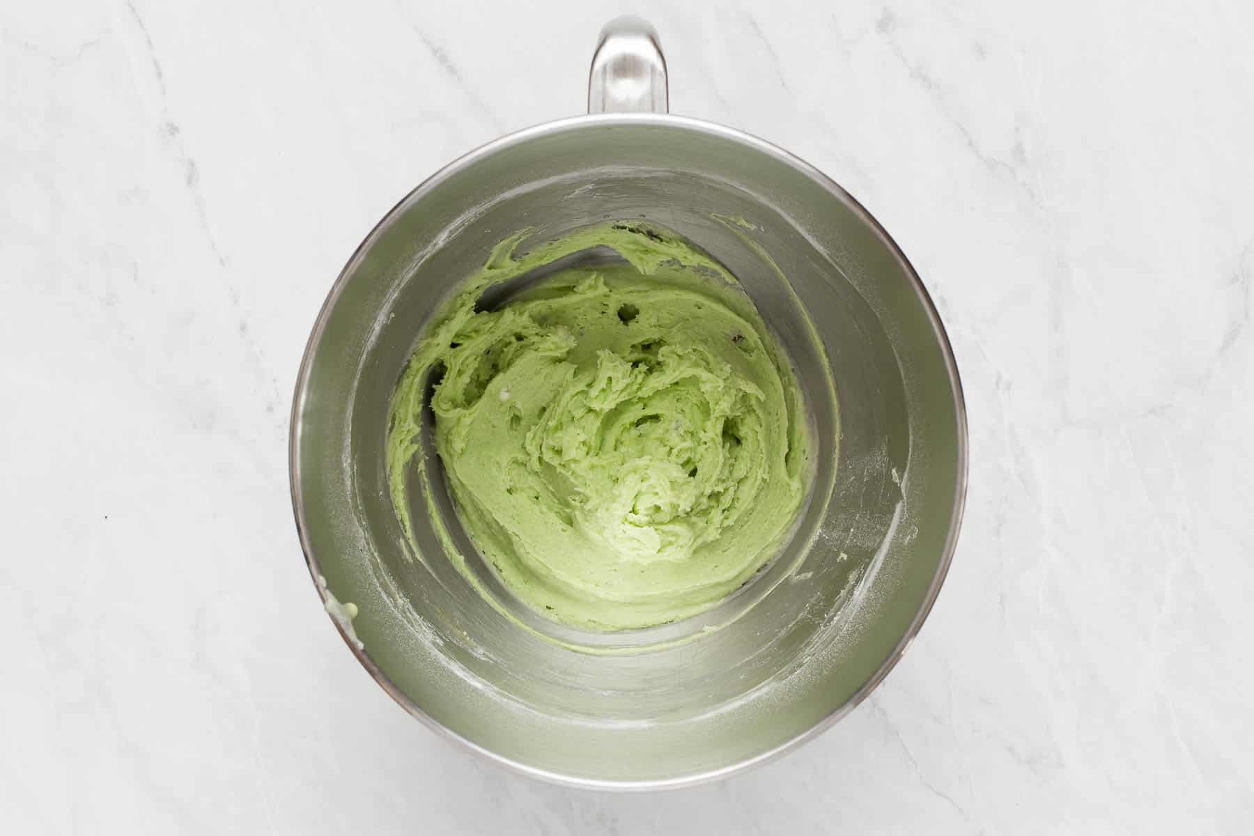 Bright green pistachio pudding cookies batter in metal mixing bowl.