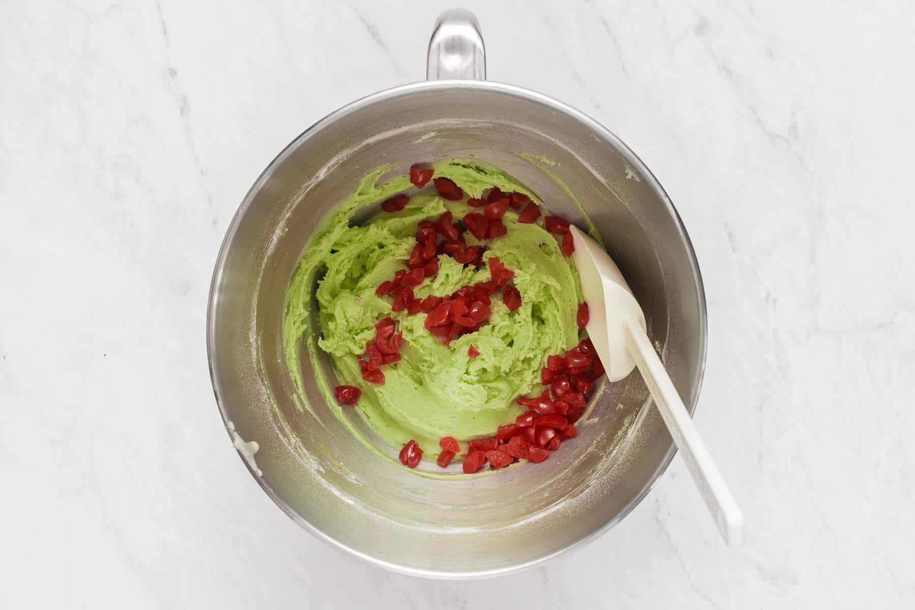Stirring bright red cherries into green dough.