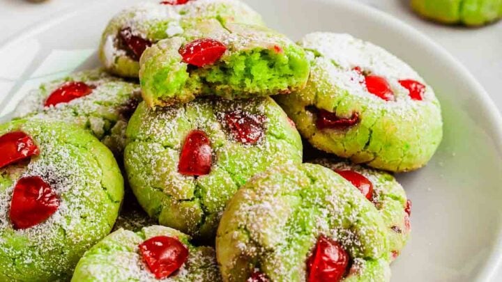 Plate of bright green pistachio pudding cookies with red cherries studded throughout.