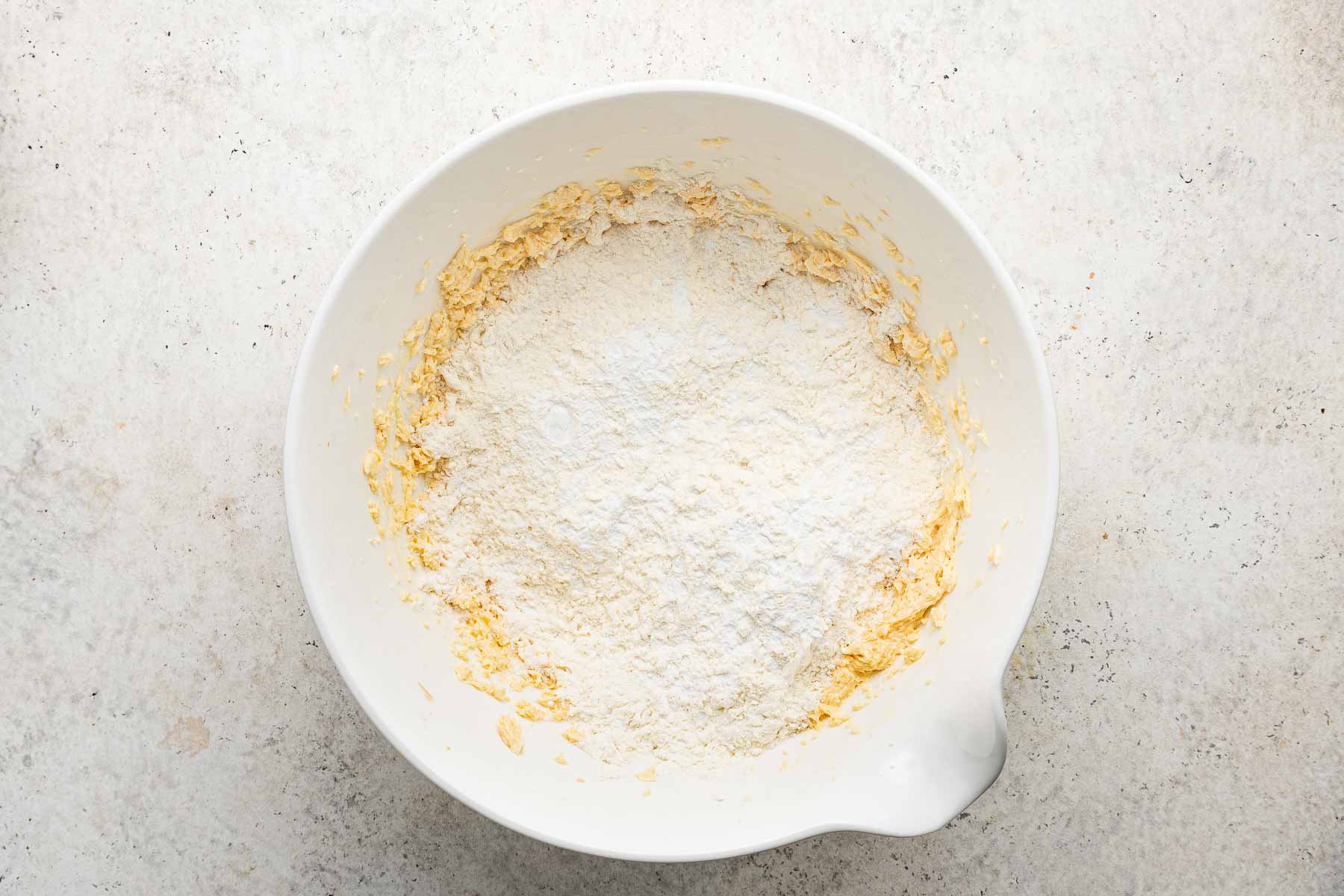 White mixing bowl with flour sprinkled on top of raw yellow dough.