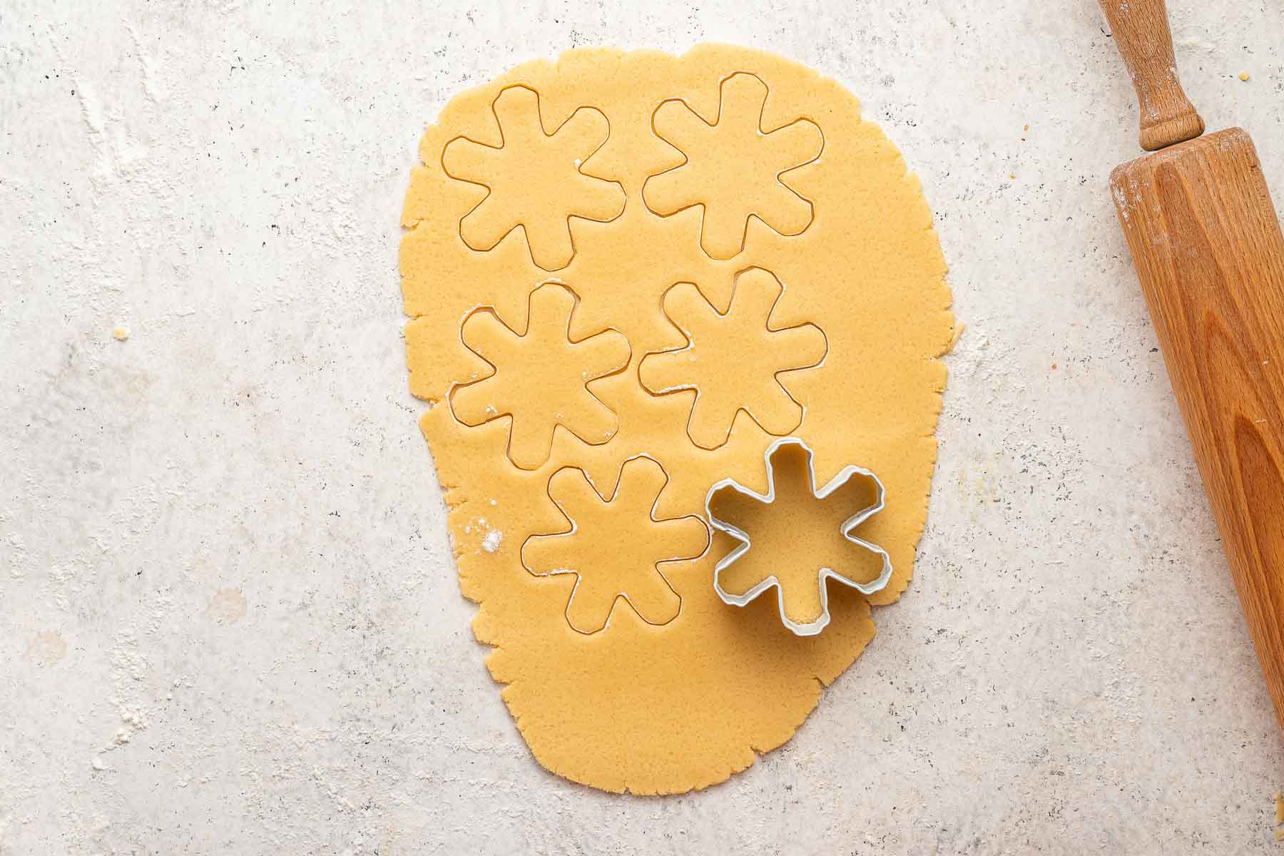 A snowflake cookie cutter being used to cut out raw sugar cookie dough.