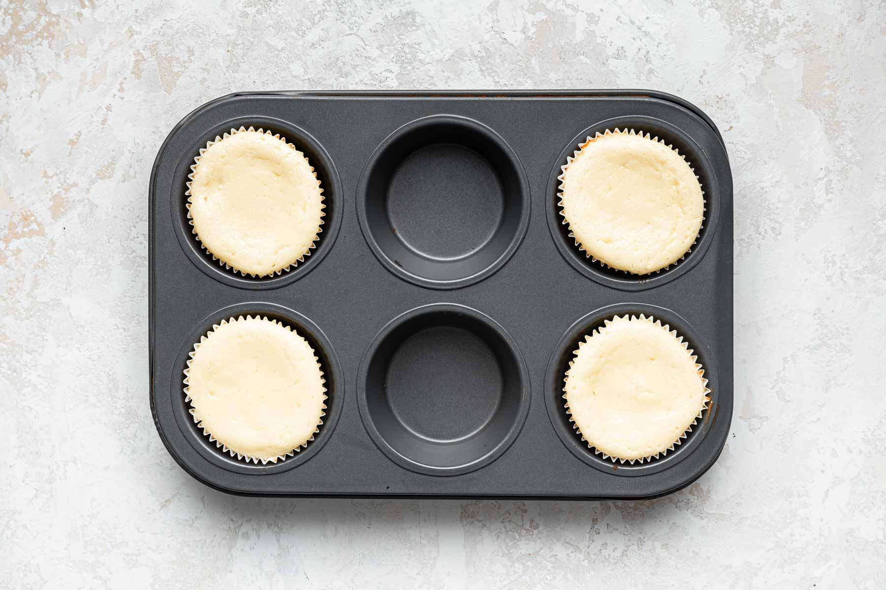 Four white cheesecakes baked in a muffin pan.