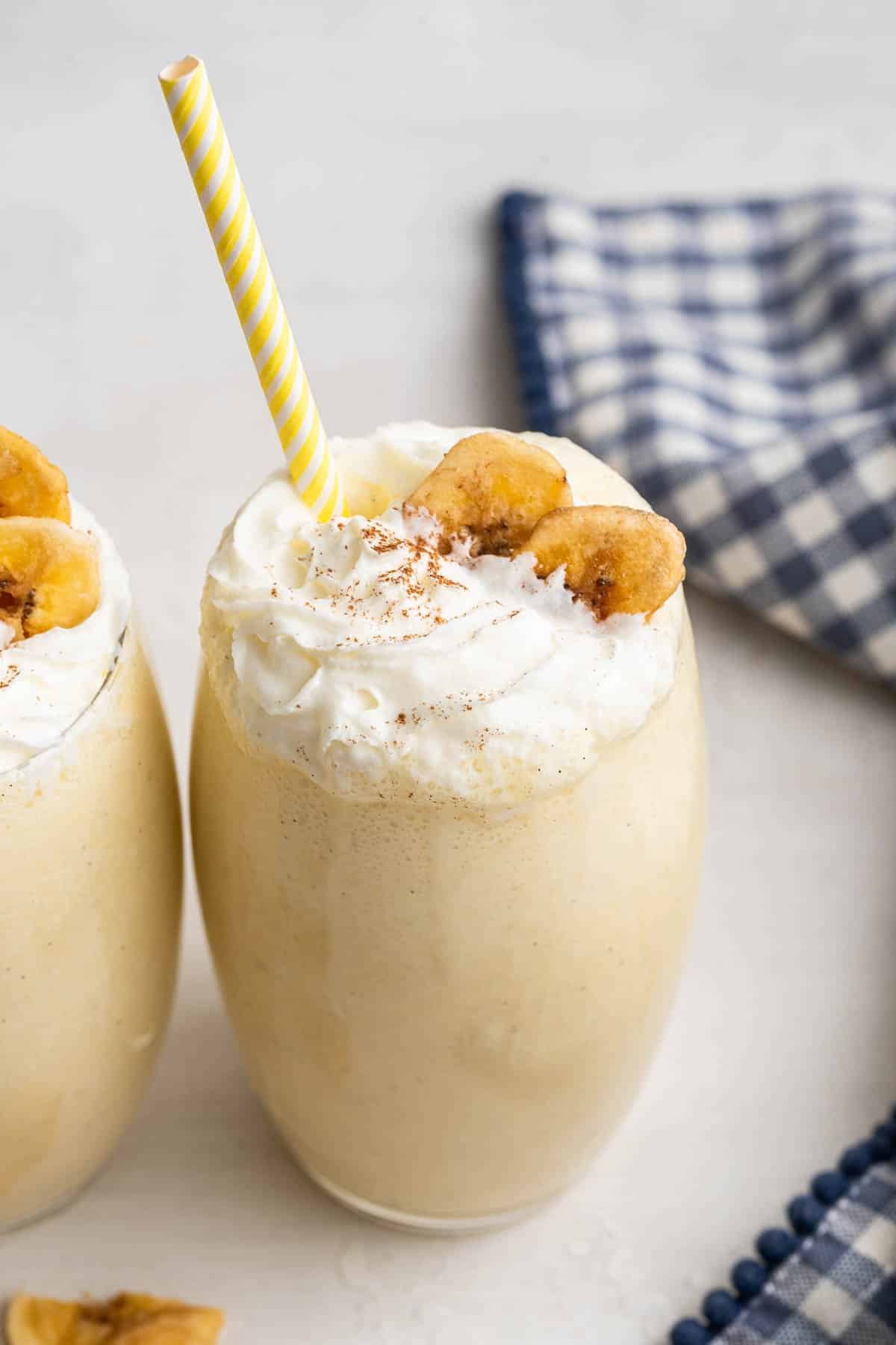 Overhead shot of two banana milkshakes garnished with whipped cream, banana chips and a straw.