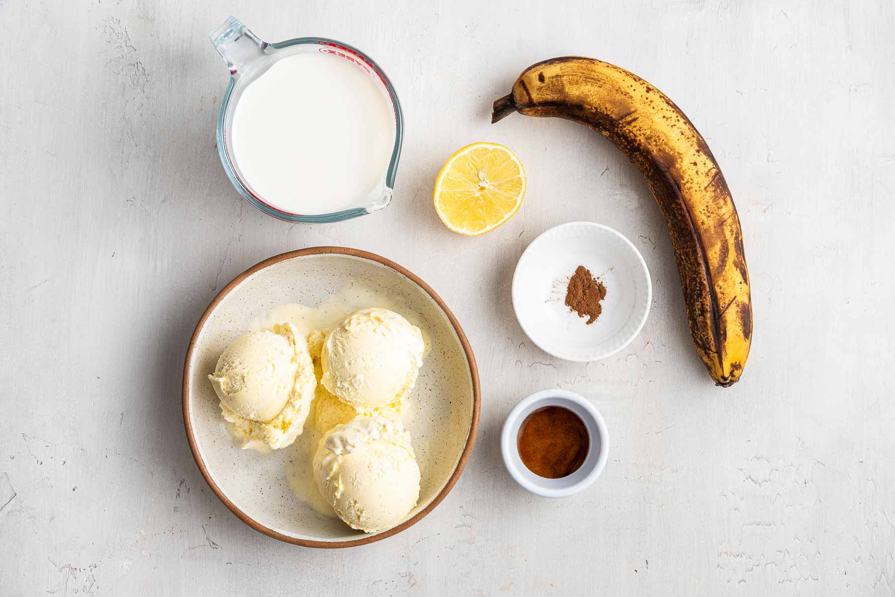Bowl with scoops of ice cream, one banana, vanilla and milk on grey countertop.