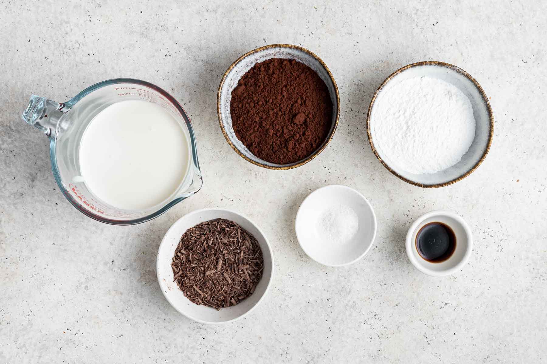 Ingredients for chocolate whipped cream in small bowls on marble counter.