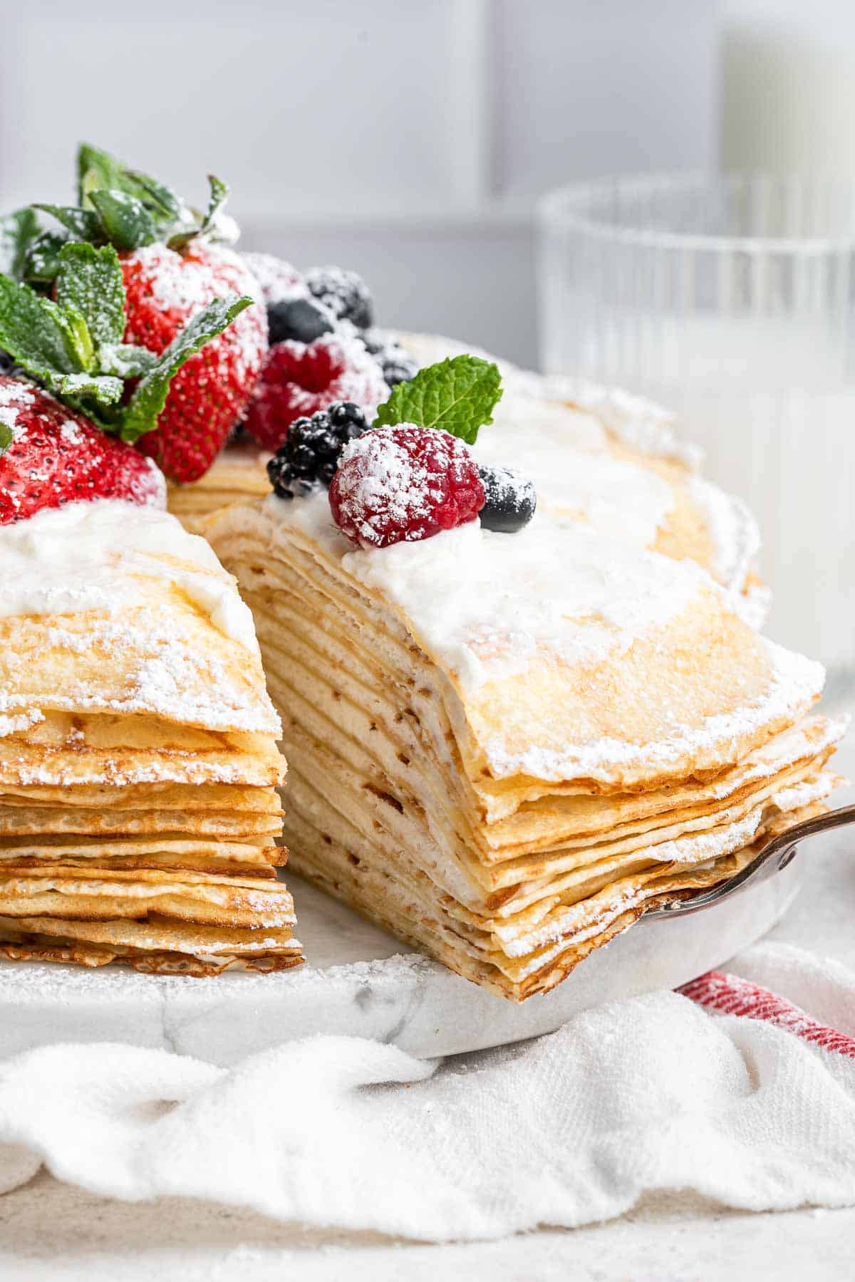 A slice of crepe cake being removed from a whole cake with fresh berries on top.